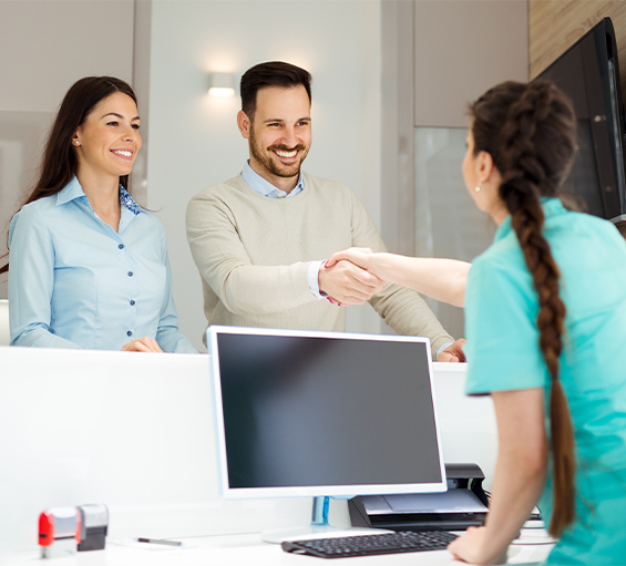 Dental receptionist shaking hands with patient at front desk